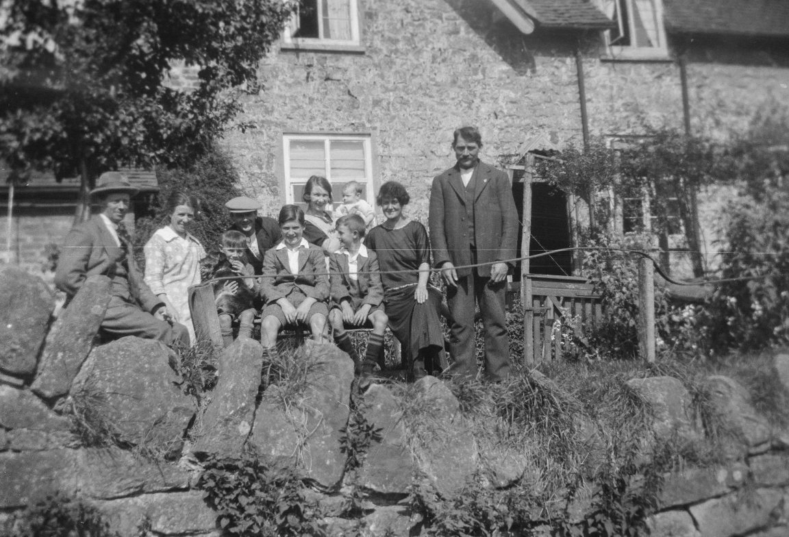 A scratched black and white photograph of a family outside a stone cottage